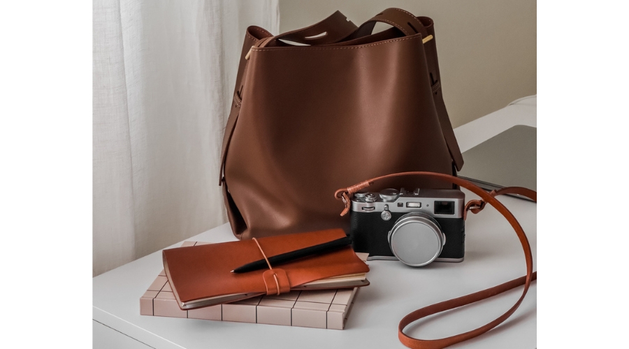 Leather tote bag, notebooks, camera on a white table