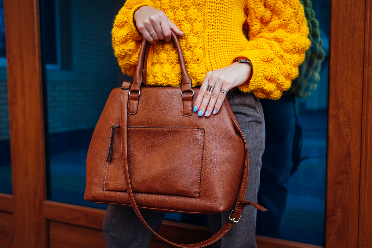 Woman holding stylish bag and wearing yellow sweater 